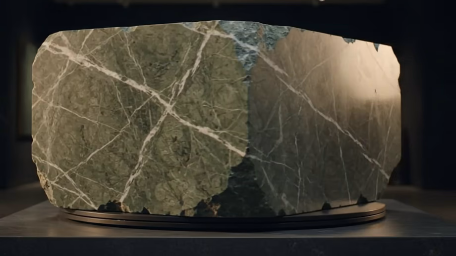 Green marble block on a turntable, turned to a raking angle so light travels across the veining and along the sawn edge